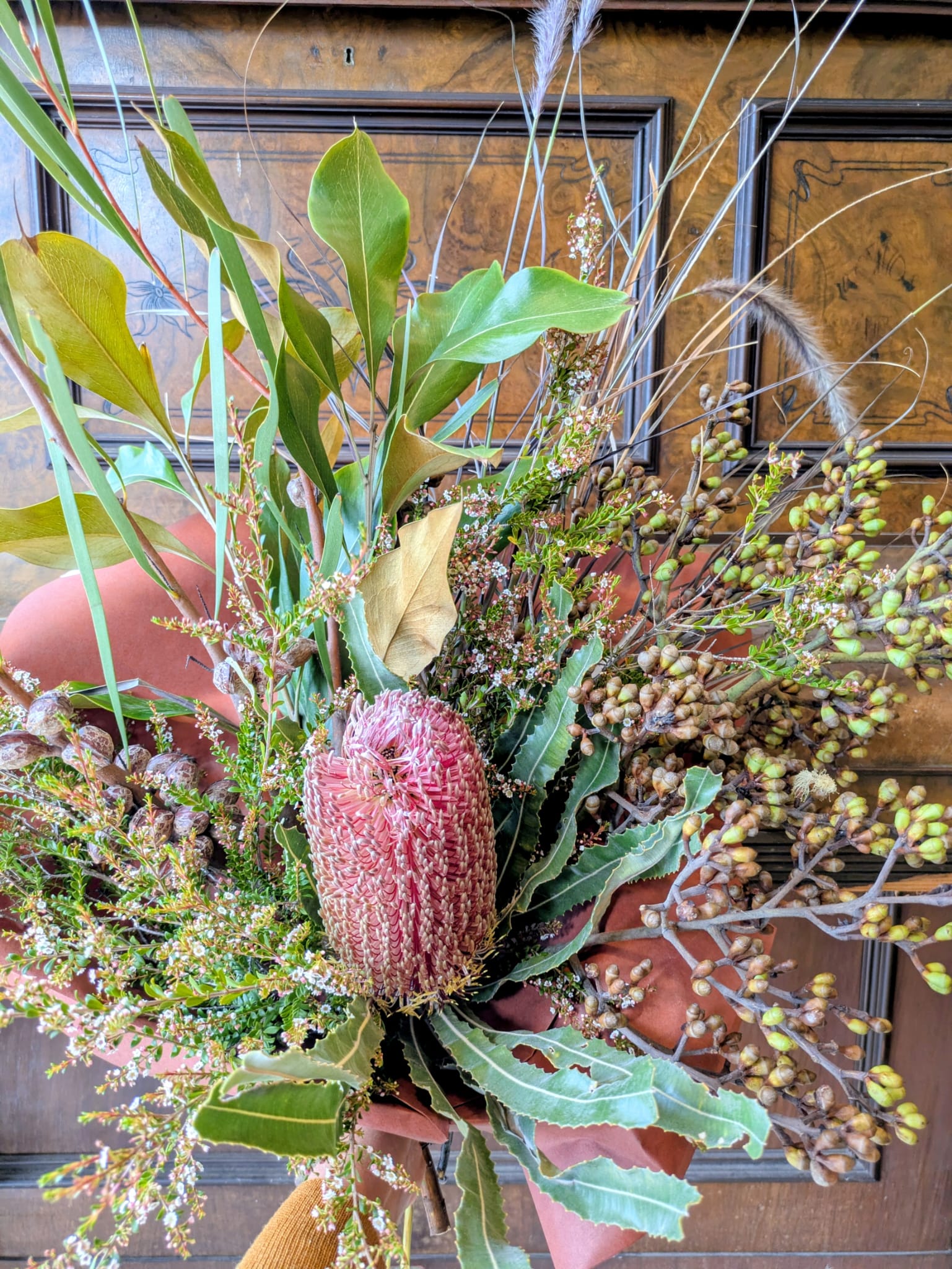Hand holding a bouquet of native Australian flowers in front of a wooden background