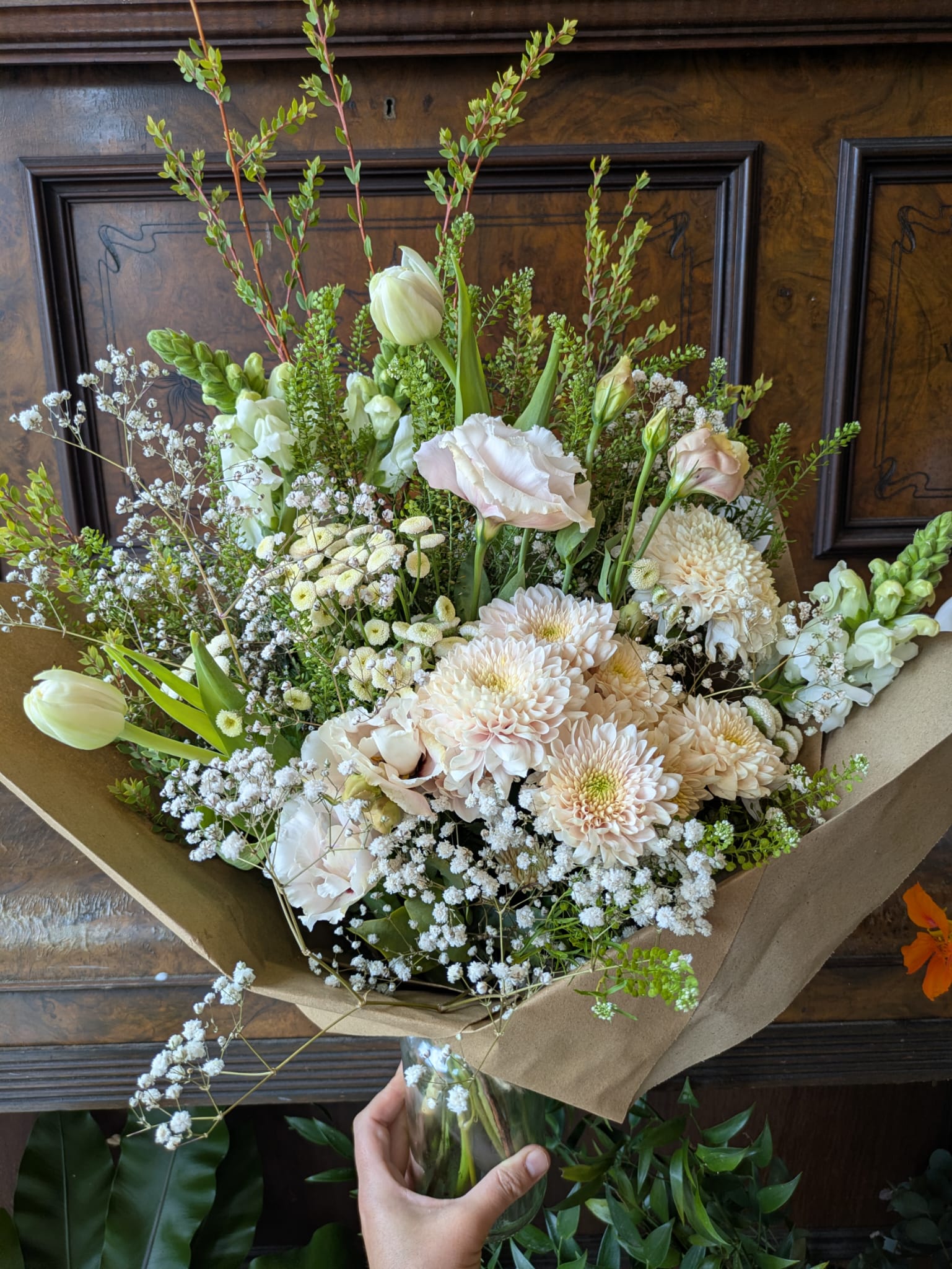 Bouquet of white flowers with greenery on brown paper against a wooden background